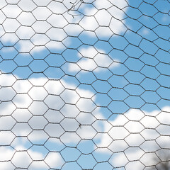 Fototapeta na wymiar twisted wire fence against a cloudy blue sky