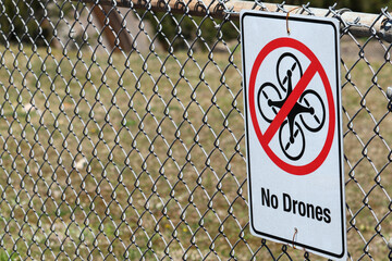 No drones warning sign on chain link fence on cloudy day