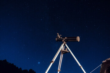 Black telescope reflector on a tripod under the starry dark blue night sky