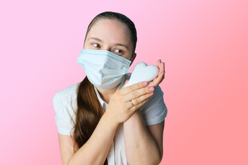 girl in white blouse and a medical mask holding heart model in her hands, symbol of love, concept of confession, Valentine's Day, cardiology