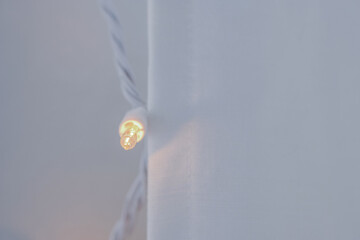 Horizontal image of Soft linen curtains cover soft christmas holiday lights inside a home