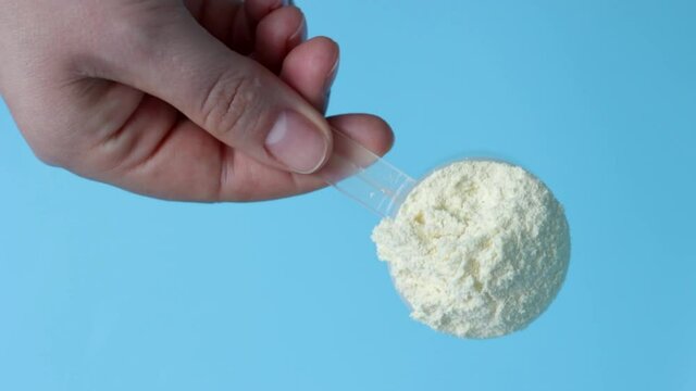 Female hand holding scoop with protein powder on a blue background.