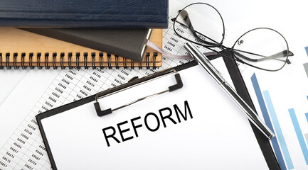 Text REFORM on Office desk table with notebooks, supplies,analysis chart, on the white background.