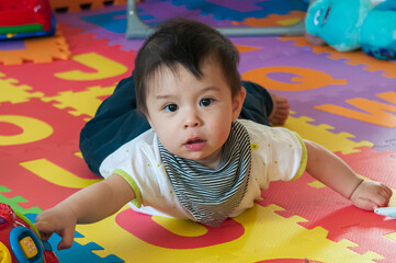 Closeup shot of a cute Swiss baby boy playing with toys on a rubber mat