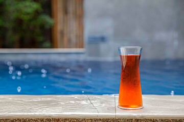 Cool tea in a glass bottle placed at the edge of the swimming pool in the house