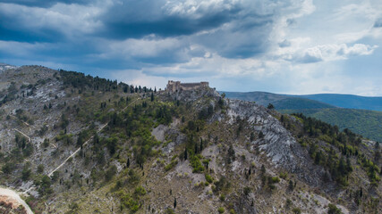Fototapeta na wymiar Aerial drone view of fortress fortress on a cliff on cloudy day. Old castle on the hill, view from above. Historic town Blagaj in Bosnia and Herzegovina. Stjepan-grad. 