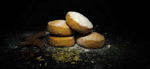 Fototapeta na wymiar Closeup of a Home Made Baked Wheat Cookies or Biscuits stacked in a isolated black background. Flavor of Cinnamon, Fennel seeds, clove and sprinkle of Sugar Powder. Bakery. Pastry. Food Photography