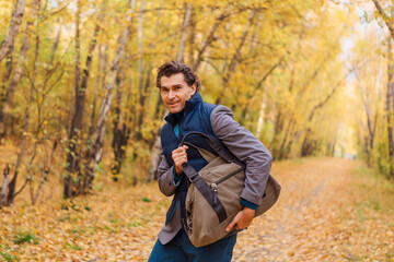 Tall handsome man with a bag in the autumn alley