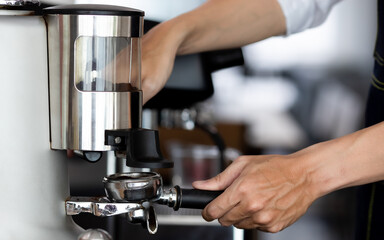 close up photo of male hands holding a metal tamper and a portafilter with coffee in a coffee shop. A man barista preparing for pressing ground coffee for brewing espresso or americano in a cafe.