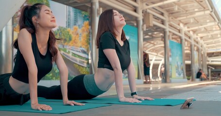 group of beautiful young fitness women doing yoga stretching arm and leg or head to knees in urban outdoors . two friend sport girl exercise together . workout healthy lifestyle. City life concept .