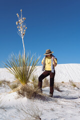 A girl-hiker and yucca plant in the white sand desert over the blue sky