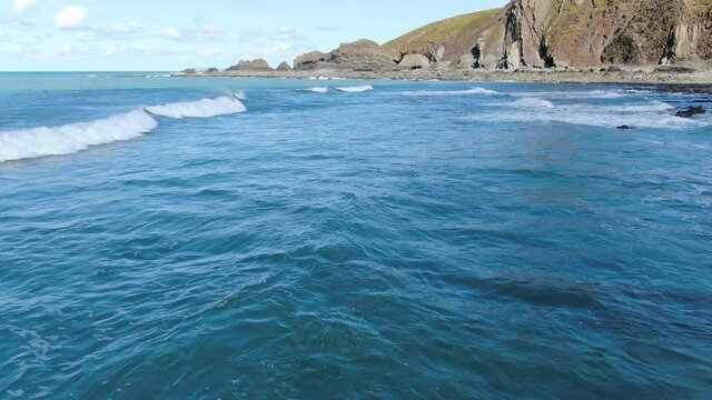 Aerial shot of the waves in the blue sea at Spekes Mill coastal beach in Devon