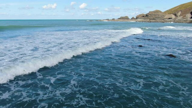 Aerial shot over the waves in the sea at Spekes Mill coastal beach in Devon