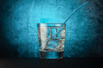 glass glass with mineral water with ice, and a drinking tube, on a dark background with a light spot in the center