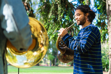 latin man playing the french horn in a park rehearsing with his band