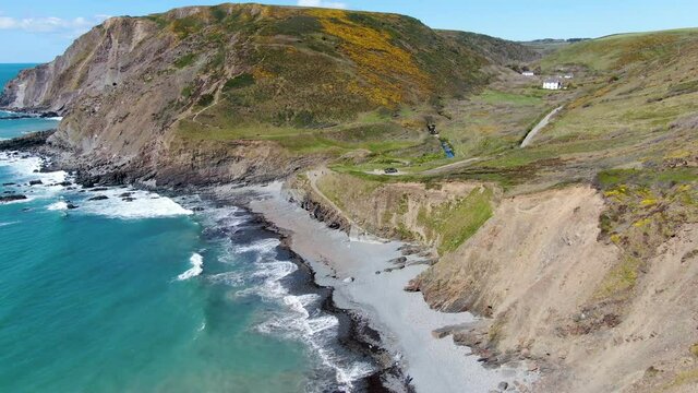 Aerial coastal shot of the waves in the sea at Spekes Mill beach in Devon near a carpark and green hills