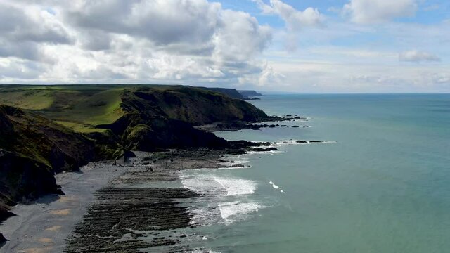 Aerial coastal shot of the waves in the sea at Spekes Mill beach in Devon showing green hills