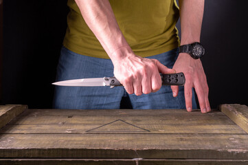 The man is holding a large folding knife. A man in jeans and a T-shirt. - obrazy, fototapety, plakaty