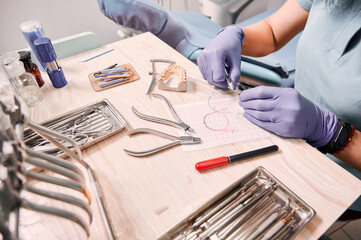 Close up view of female dentist in sterile gloves cutting braces wire while sitting at the table...
