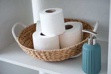 Basket with rolls of toilet paper and bottle of soap on shelf in bathroom