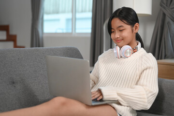 Young woman with headphone sitting on sofa and surfing internet on laptop.