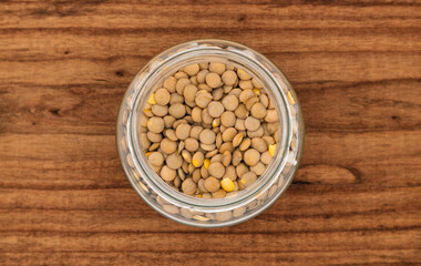 Top view of a transparent glass jar with lentils inside. Detailed view of lentils on a table or wooden surface.