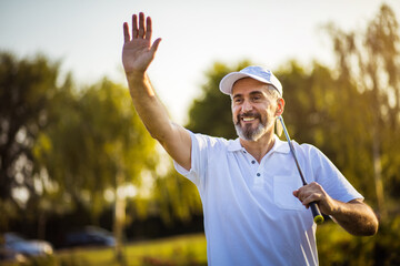 Senior golfer on golf court waving to someone.  Smiling golfer.