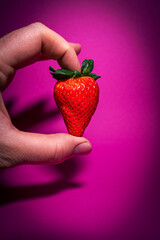 Tasty strawberry in hand with pink background