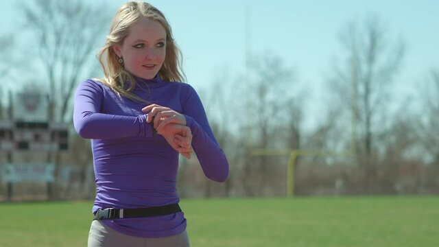 Teen girl runner checks her time on her watch after a run in her cool down walk after a run on the track.