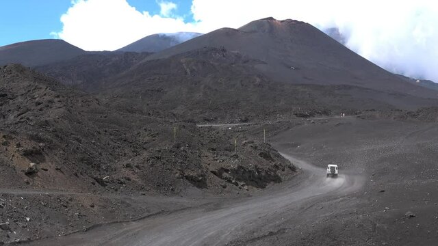 Off-road vehicle driving people to the top of Mount Etna and back, on a volcanic path. Smoke and clouds, 4k footage