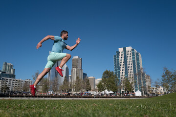Fototapeta na wymiar Full length of healthy man running and sprinting outdoors near city skyline. Male urban runner. Dynamic jump movement.