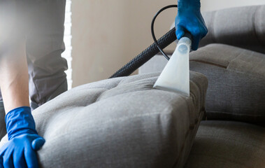 Cleaning service. Man janitor in gloves and uniform vacuum clean sofa with professional equipment