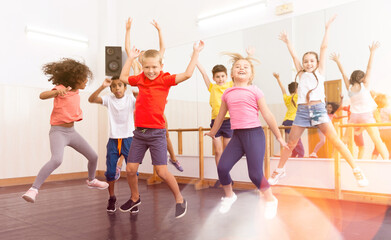 Obraz premium Group of happy sporty kids with female teacher training in modern dance studio, jumping together
