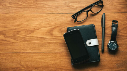 Top view of notebook,mobile phone.glasses,pen and watch on wooden background with copy space.