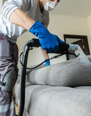 Cleaning service. Man janitor in gloves and uniform vacuum clean sofa with professional equipment