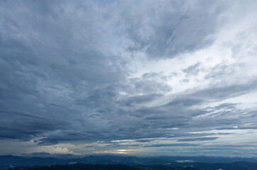 A view of a large mountain under gloomy clouds with raining in distant sky background cloudy wallpaper