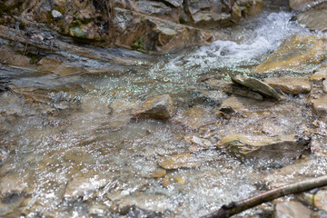 mountain blue water flows down from gray stones waterfall in summer close-up