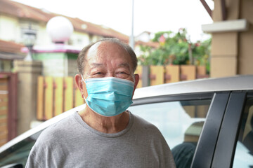 Fototapeta na wymiar Senior Asian man with medical face mask on, standing outside his home. Stay indoors during pandemic concept.