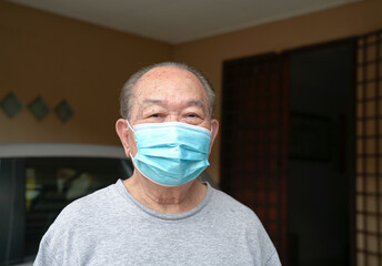 Senior Asian man with medical face mask on, standing outside his home. Stay indoors during pandemic concept.