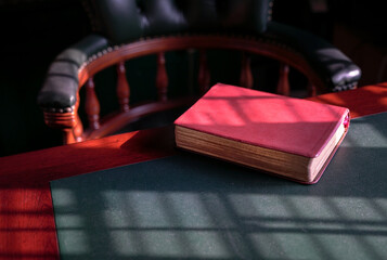 Closed bible on the edge of table in a study room with chesterfield chair at the background. Copy space.