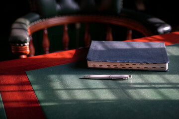 Bible on the edge of study table with chesterfield chair at the background. 