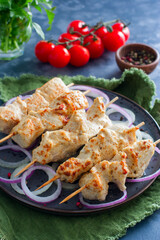 Chicken skewers on wooden skewers with vegetables on a ceramic plate, selective focus