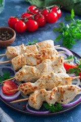 Chicken skewers on wooden skewers with vegetables on a ceramic plate, selective focus