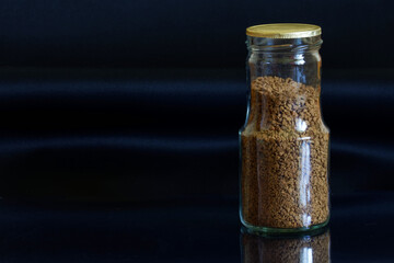 Transparent glass, sealed with foil, jar with instant coffee on a dark background. Free space for...