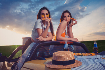 Charming girls eating pizza, posing in yellow car roadster with french fries, hat and soda in glass...