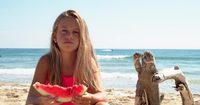 Smiling 9 years old girl eating watermelon on the beach. Child eating tasty summer fruit. Happy summer time. 4k slow motion