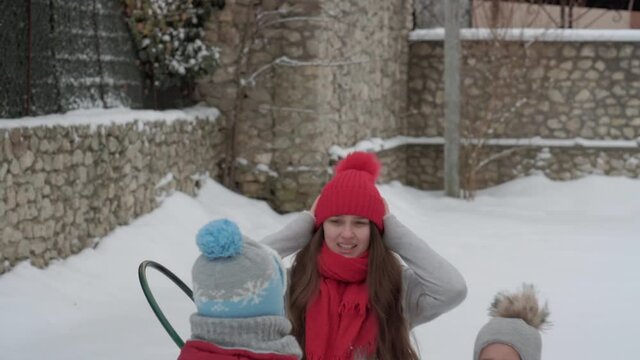 vacation, game, family concept - slo-mo authentic three happy preschool toddler kids siblings with young wonan mom sledding and play with snow. snowfall in cold season weather in winter yard outdoors