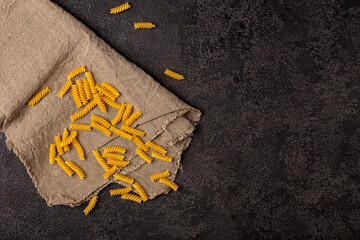 Burlap napkin on a dark structural background, top view. A scattering of macaroni on it.