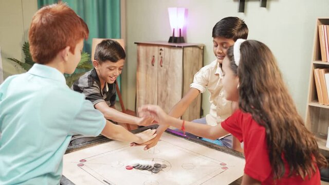 Group of kids fighting to decide for pair to play carrom by clapping or flipping hands on carrom board at home - Concept of childhood holiday lifestyle and summer vacation.