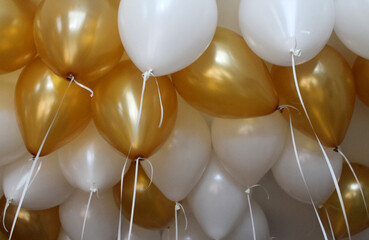 Balloons filled with helium, white and gold colors with white ribbons fly under the ceiling. Flying balls, as an essential accessory for celebrating birthdays and other holidays.